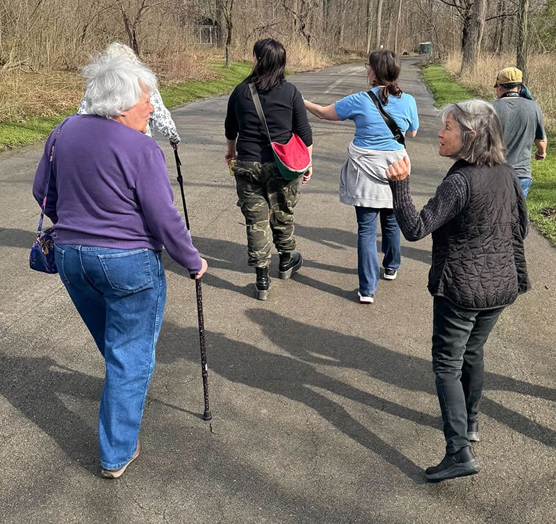 a group of women walking near trees, one with a cane